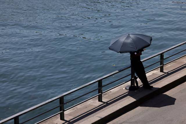 A person shelters from the sun under an umbrella along the banks of the River Seine in Paris as temperatures rise during a heatwave affecting a large part of France, June 22, 2026. REUTERS