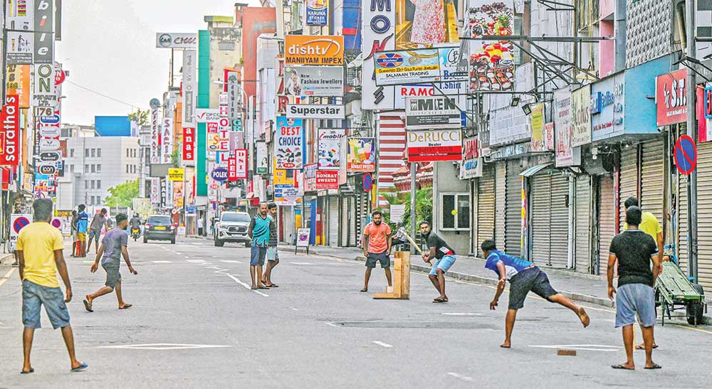 Youth play cricket along a road amid closed shops during a curfew in Colombo on May 11, 2022. - Nearly all of Colombo's residents had kept to their homes on May 11, as the government stepped up efforts to restore order. 	photo: AFP 