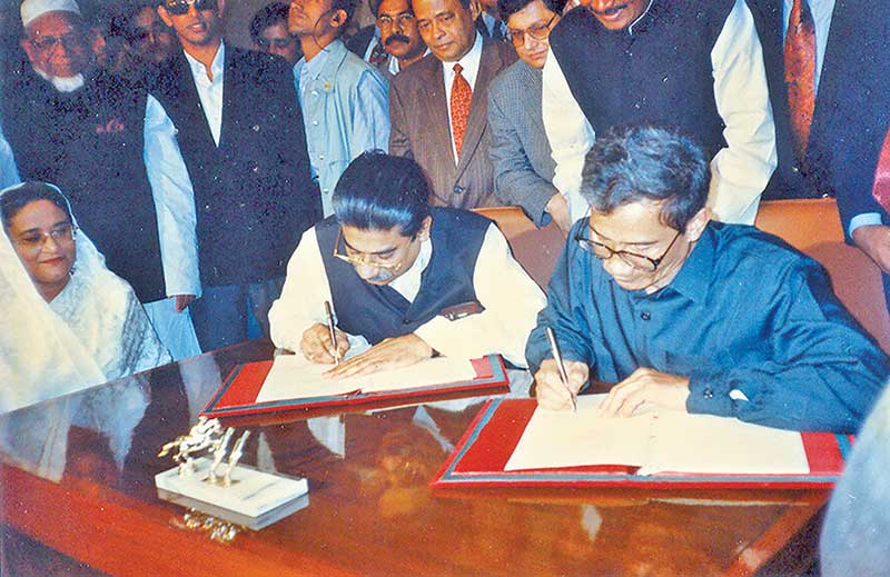 Jatiya Sangsad Chief Whip Abul Hasnat Abdullah (left) and Shanti Bahini Leader Shantu Larma signing Chittagong Hill Tracts (CHT) Peace Accord on December 2, 1997. Prime Minister Sheikh Hasina (extreme left) looks on. 	File: Photo