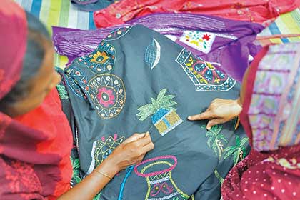 Women in Shombhari's neighbourhood stitch the motif of a hut onto a modern nakshi kantha. The hut looks like one Shombhari used to live in, she says 